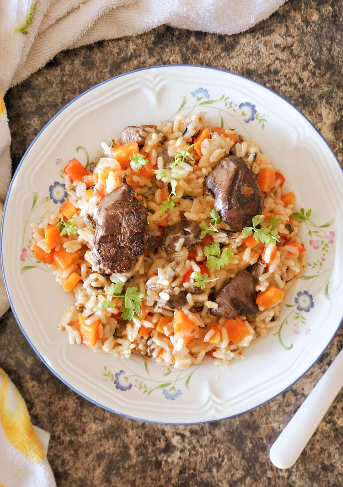 Overhead shot of a white plate with pilaf with vegetables and chicken liver.