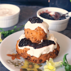 A papanas on a white plate with ramekins of sour cream and jam in the background