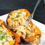 Two halves of roasted butternut squash stuffed with veggie couscous and topped with melted cheese.