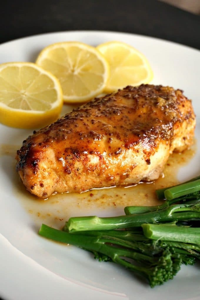 Honey Mustard Chicken Breast on a White Plate Flanked by Broccoli and 3 Lemon Slices.