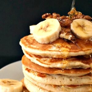 A stack of american pancakes topped with banana slices and walnuts, and drizzled with honey