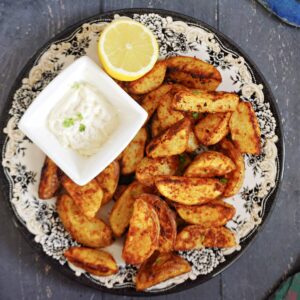 Overhead shoot of a plate with paprika potato wedges, a small bowl of mayo and half a lemon