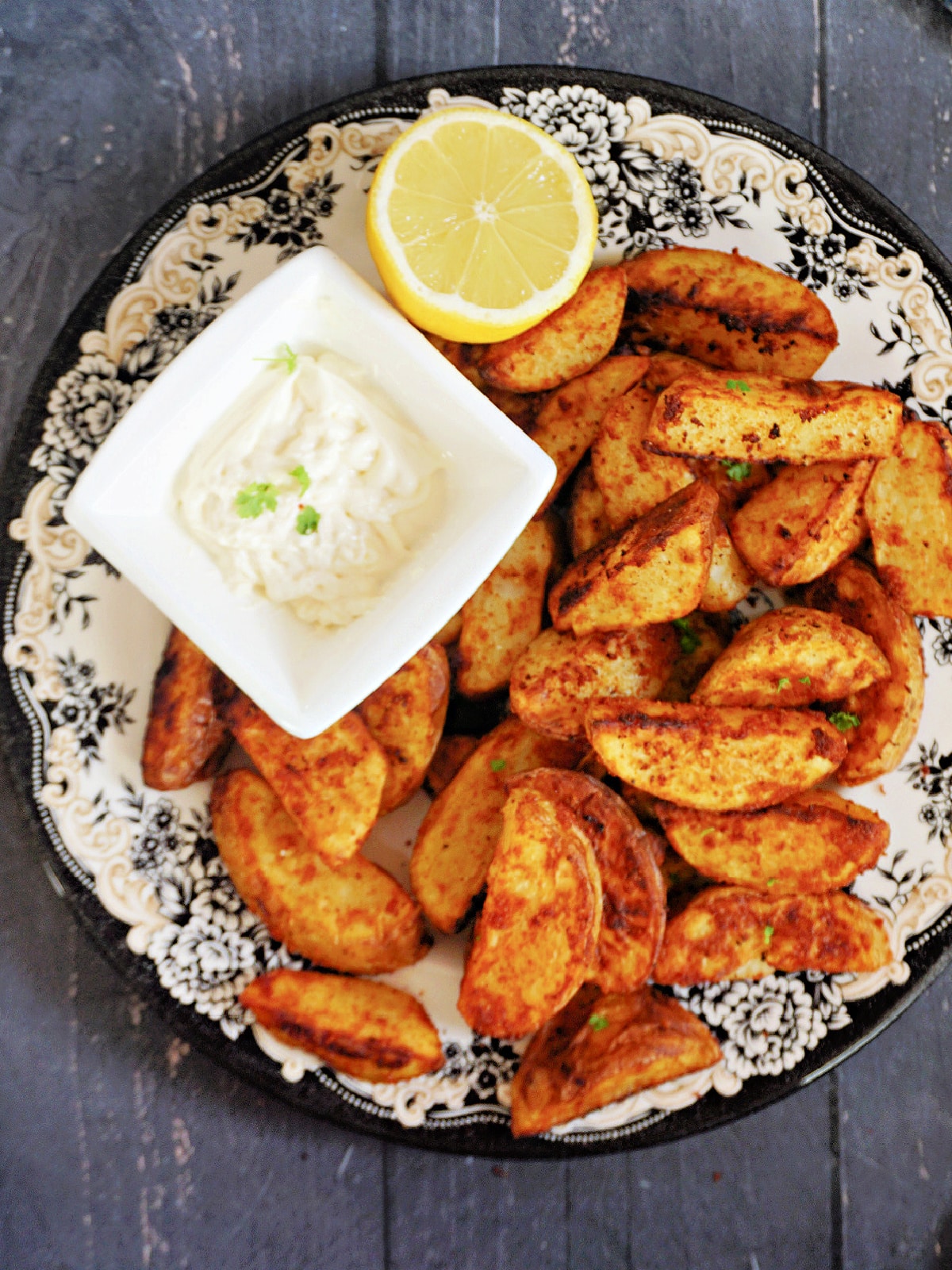 A plate with paprika potato wedges, half a lemon and a white small bowl with mayo