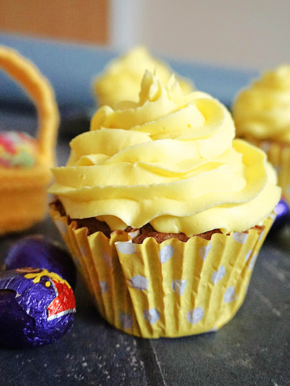 A creme egg cupcake topped with lemon buttercream and creme eggs around it