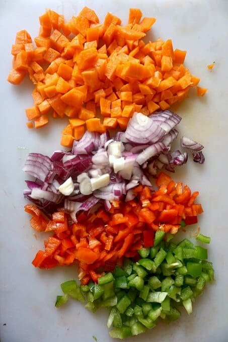 A white chopping board with chopped red onion, red pepper, green pepper and carrot for the Romanian Meatball Soup