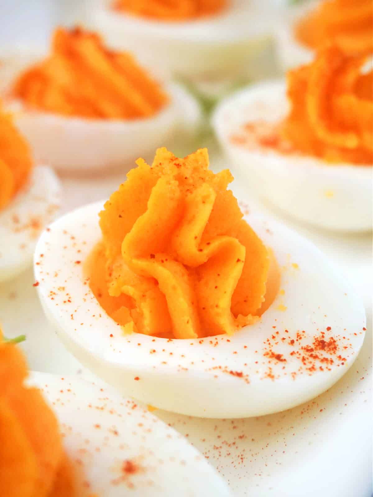 Close-up shoot of a devilled egg on a white plate with more eggs around.