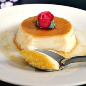 A flan on a white plate with a teaspoon slicing it