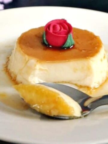 A flan on a white plate with a teaspoon slicing it