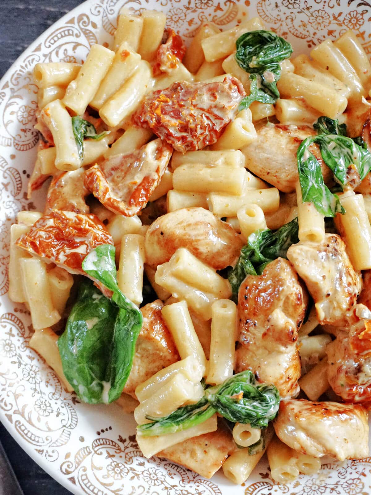 Close-up shot of a plate with pasta, spinach and sun-dried tomatoes.