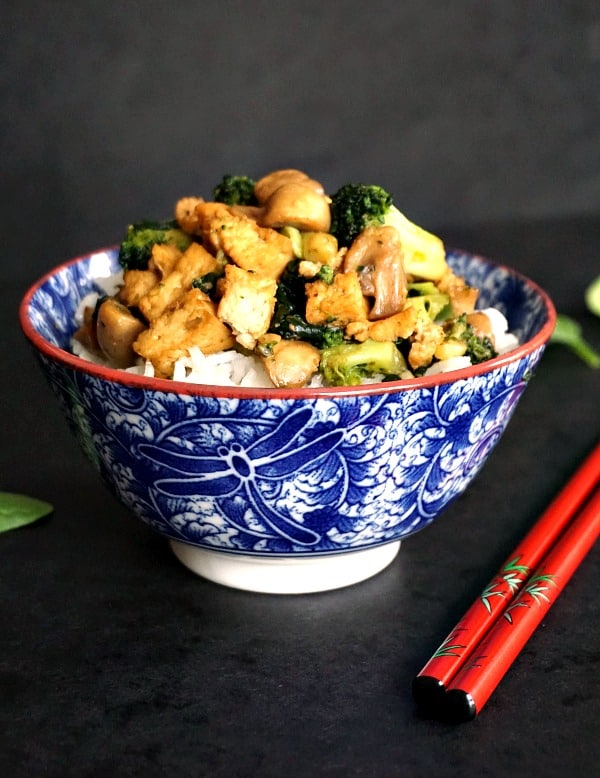 A blue bowl with tofu and broccoli stir fry, and a pair of red chopsticks on the side
