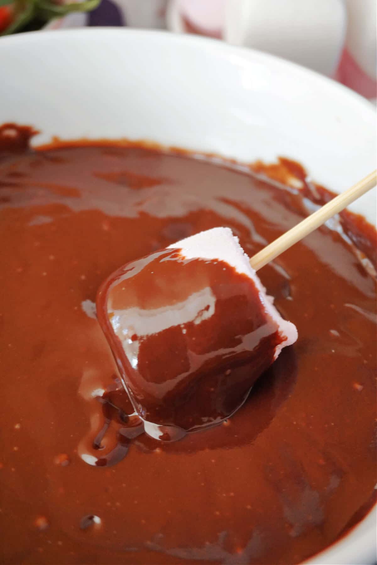 A marshmallow dipped into a bowl of chocolate sauce.