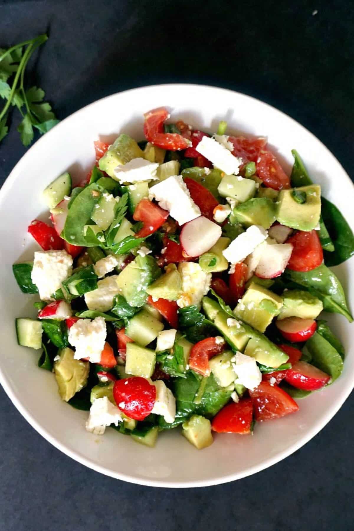 Overhead shoot of a white bowl with veggie and cheese salad.