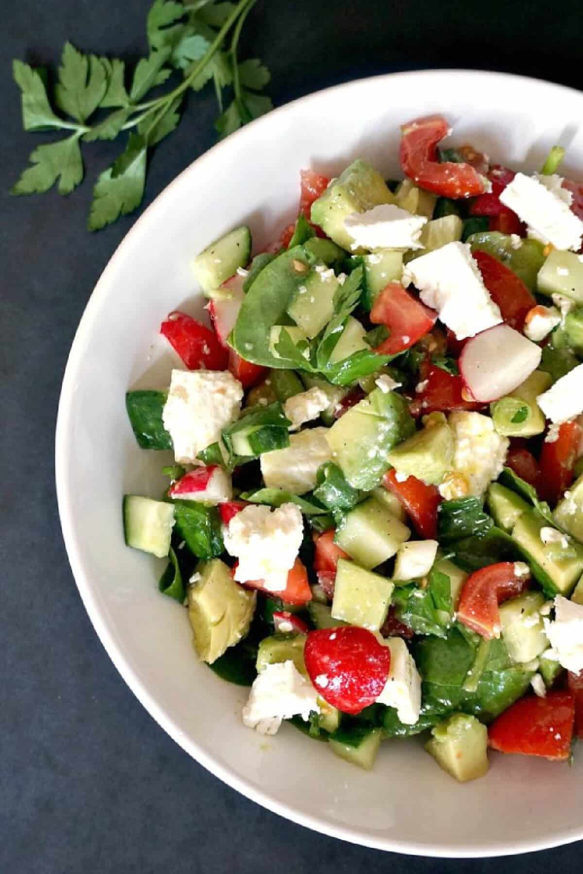 A white bowl with feta and veggie salad.