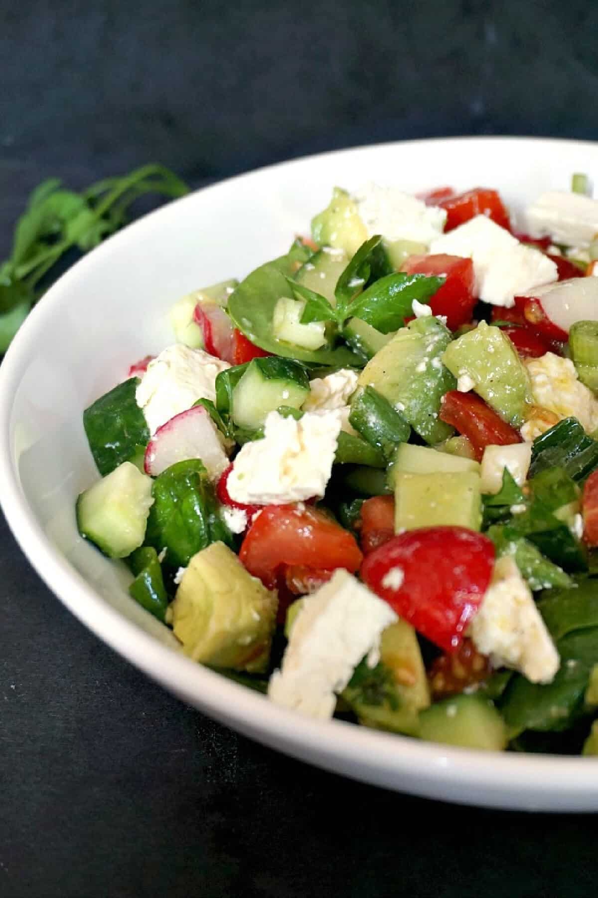 A white bowl with veggie and cheese salad.