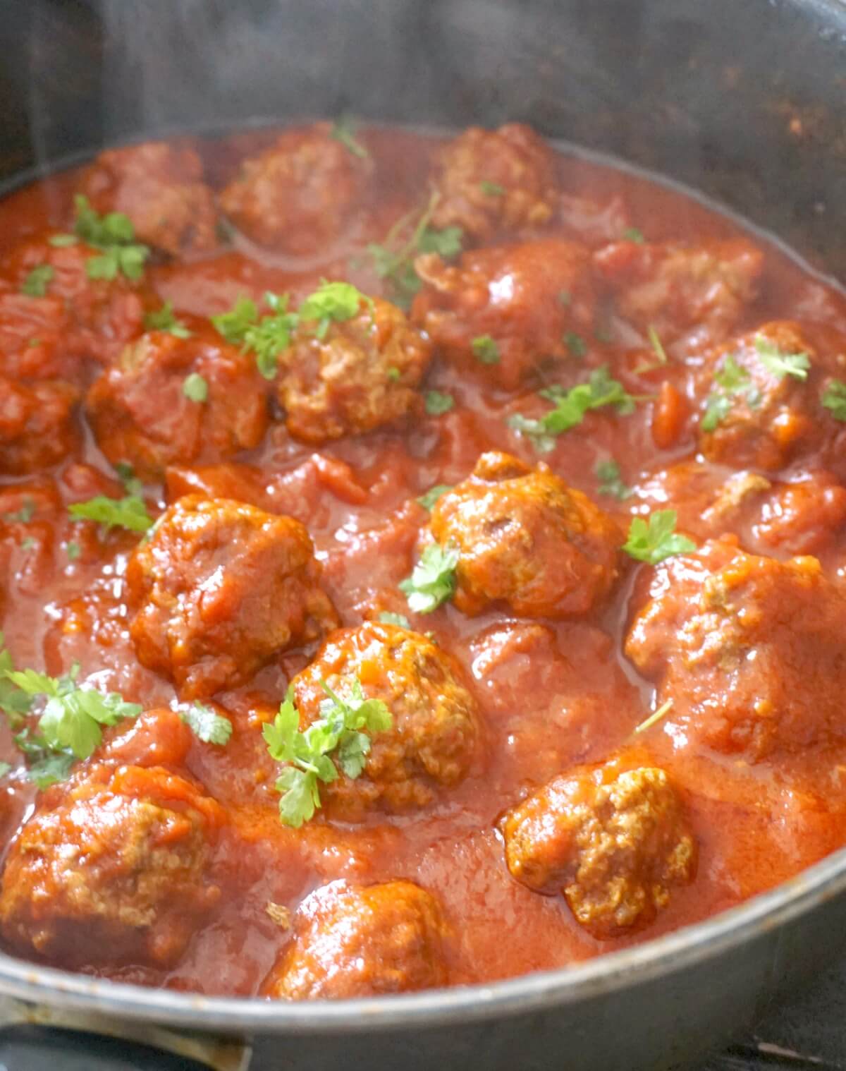 A pot with meatballs in tomato sauce garnished with chopped parsley.