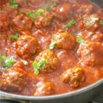A pot of meatballs in tomato sauce and parsley