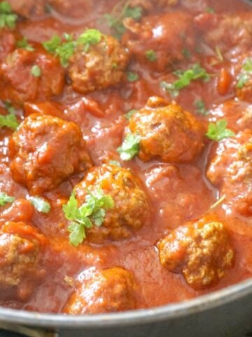 A pot of meatballs in tomato sauce and parsley