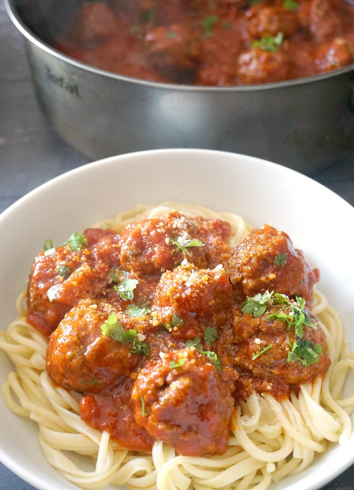 A while bowl with spaghetti topped with meatballs in tomato sauce.