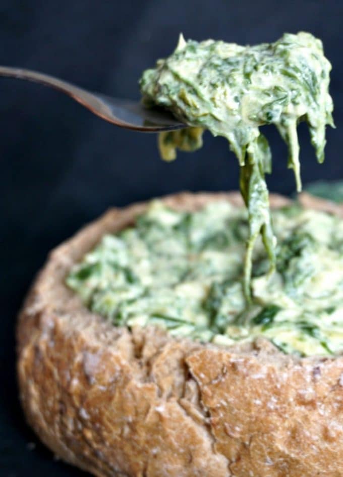 A forkful of spinach and artichoke dip over a bread bowl of dip