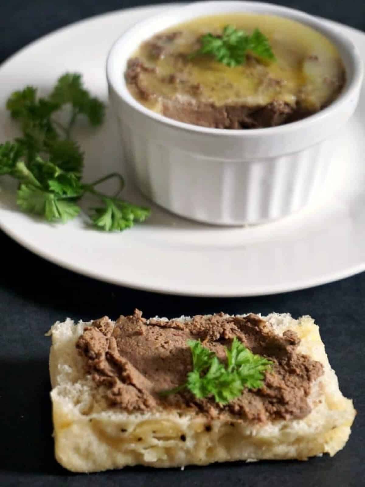 A slice of bread with liver pate and a white plate with a ramekin with more pate.