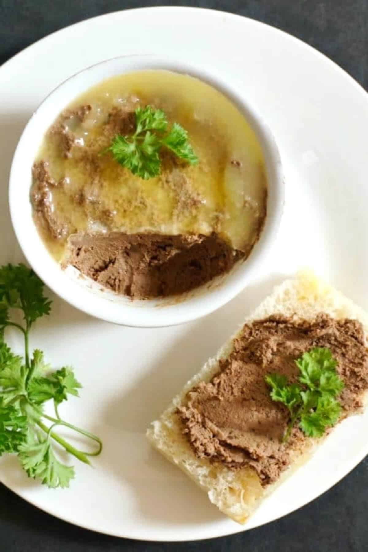 Overhead shoot of a white plate with a slice of bread with liver pate and a ramekin with more pate.