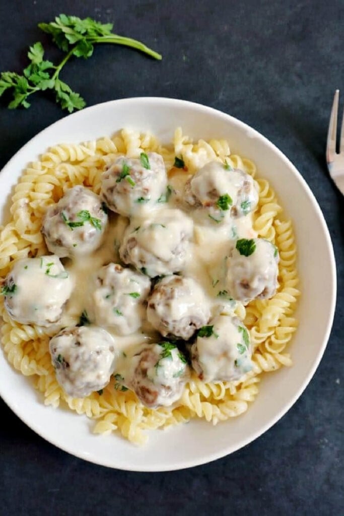 Overhead shoot of a white plate with Swedish meatballs over a bed of fusilli pasta