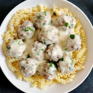 Overhead shoot of a white bowl with meatballs in white sauce over a bed of fusilli pasta