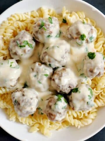 Overhead shoot of a white bowl with meatballs in white sauce over a bed of fusilli pasta