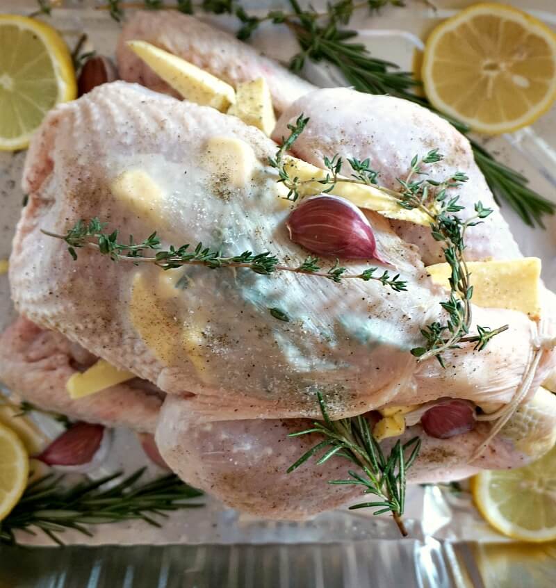Overhead photo of a whole chicken in a roasting tray with herbs and seasoning.