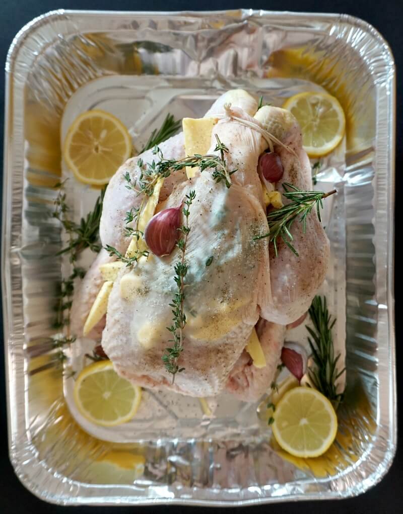 Overhead show to a whole chicken with herbs on a re-usable baking tray.