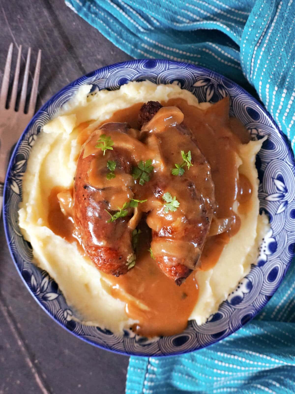 Overhead shot of a blue plate with mash, 2 sausages and gravy.