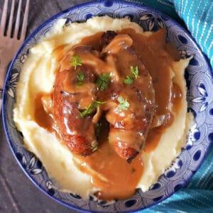 Overhead shot of a blue plate with mash topped with 2 sausages and gravy