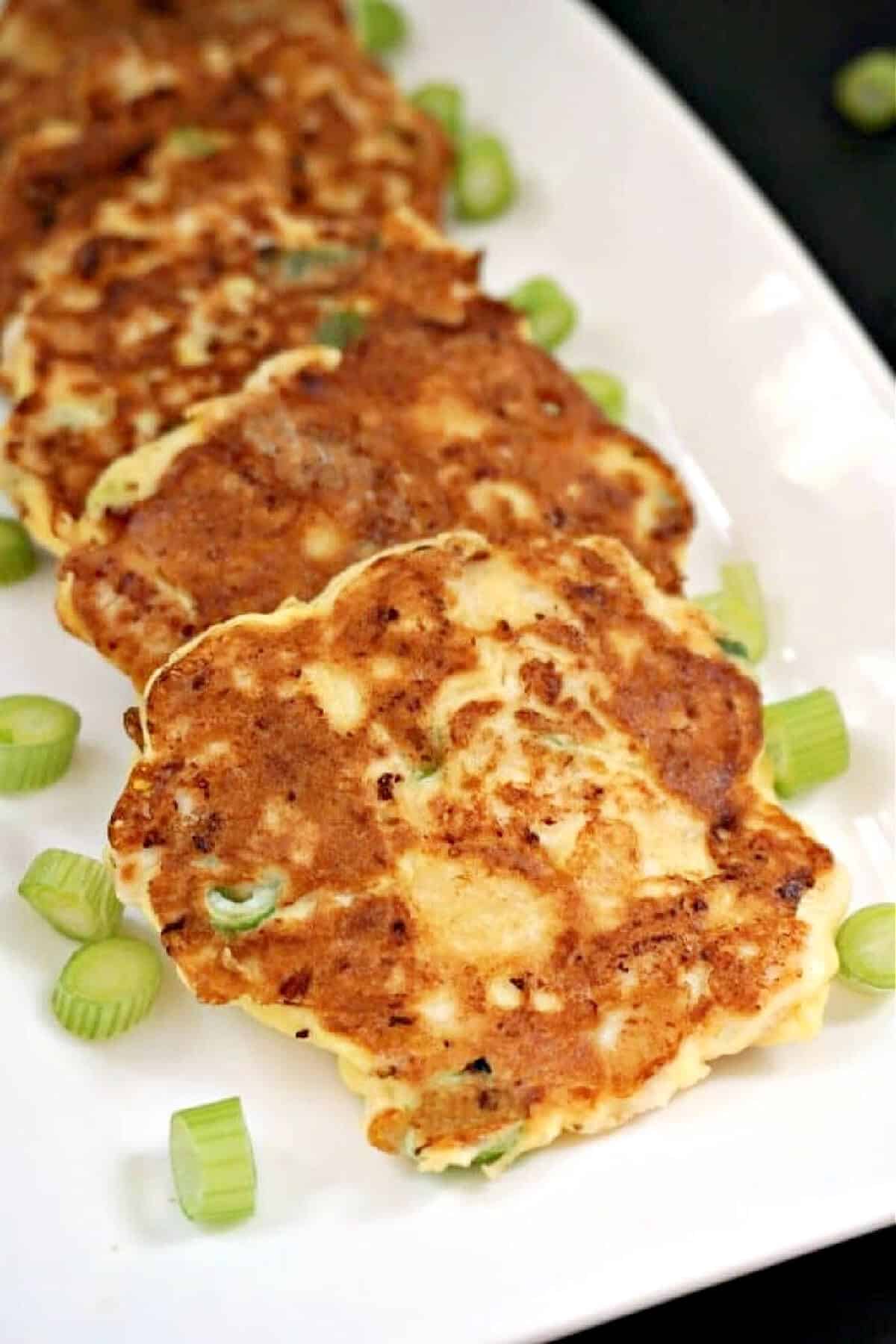 3 chicken fritters on a white plate with chopped spring onions around.