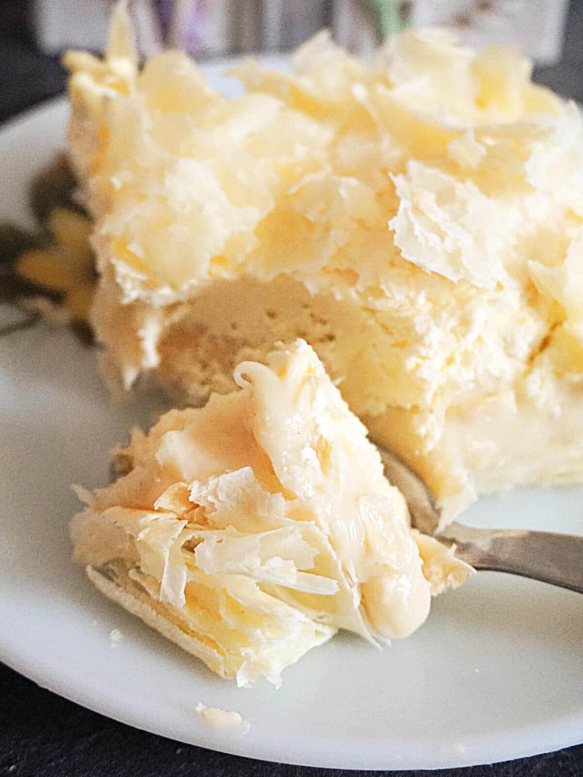 A dessert spoon cutting through a cremeschnitte slice on a white plate.