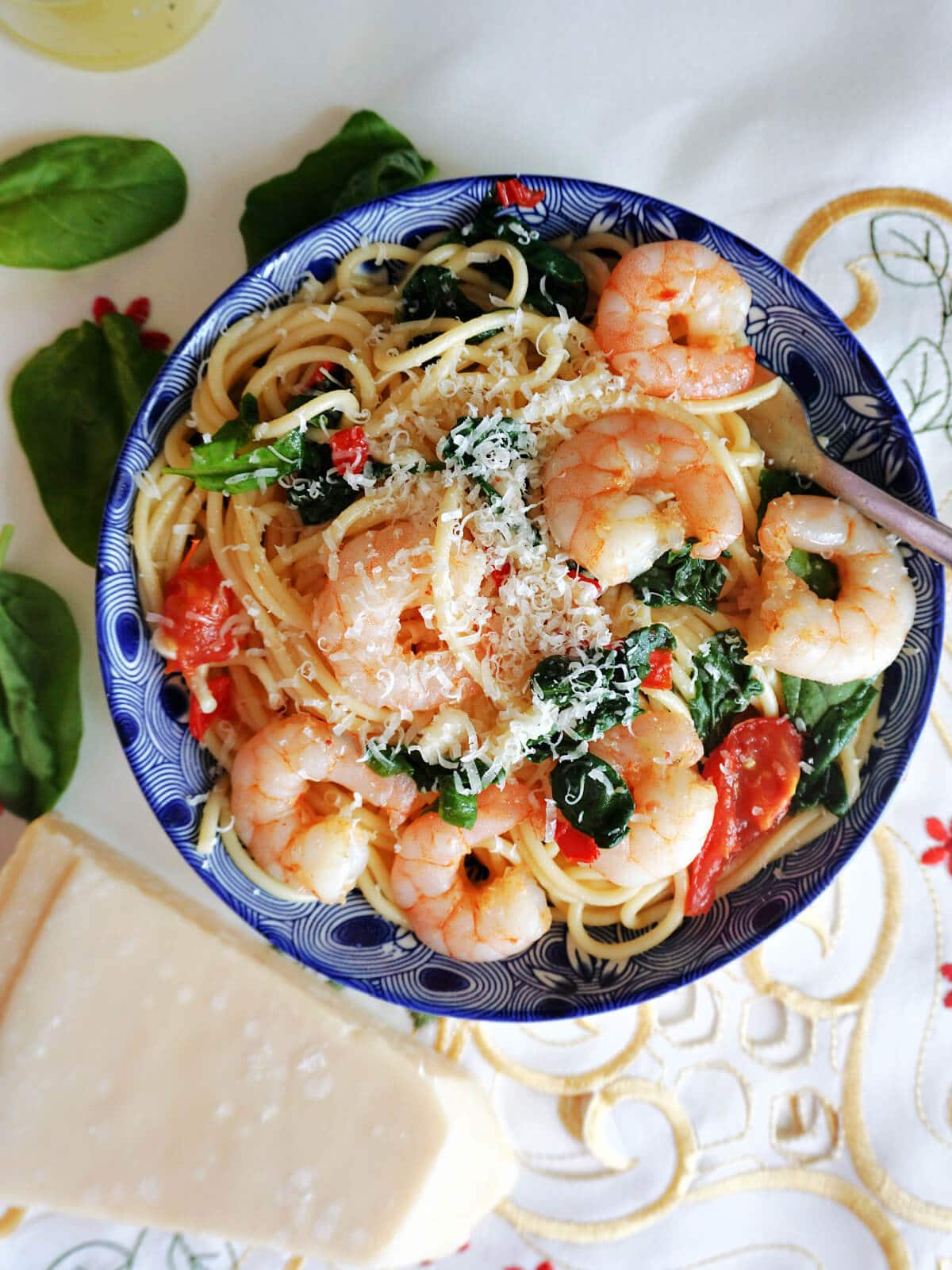 Overhead shoot of a blue plate with spaghetti, prawns, spinach and chopped tomatoes.