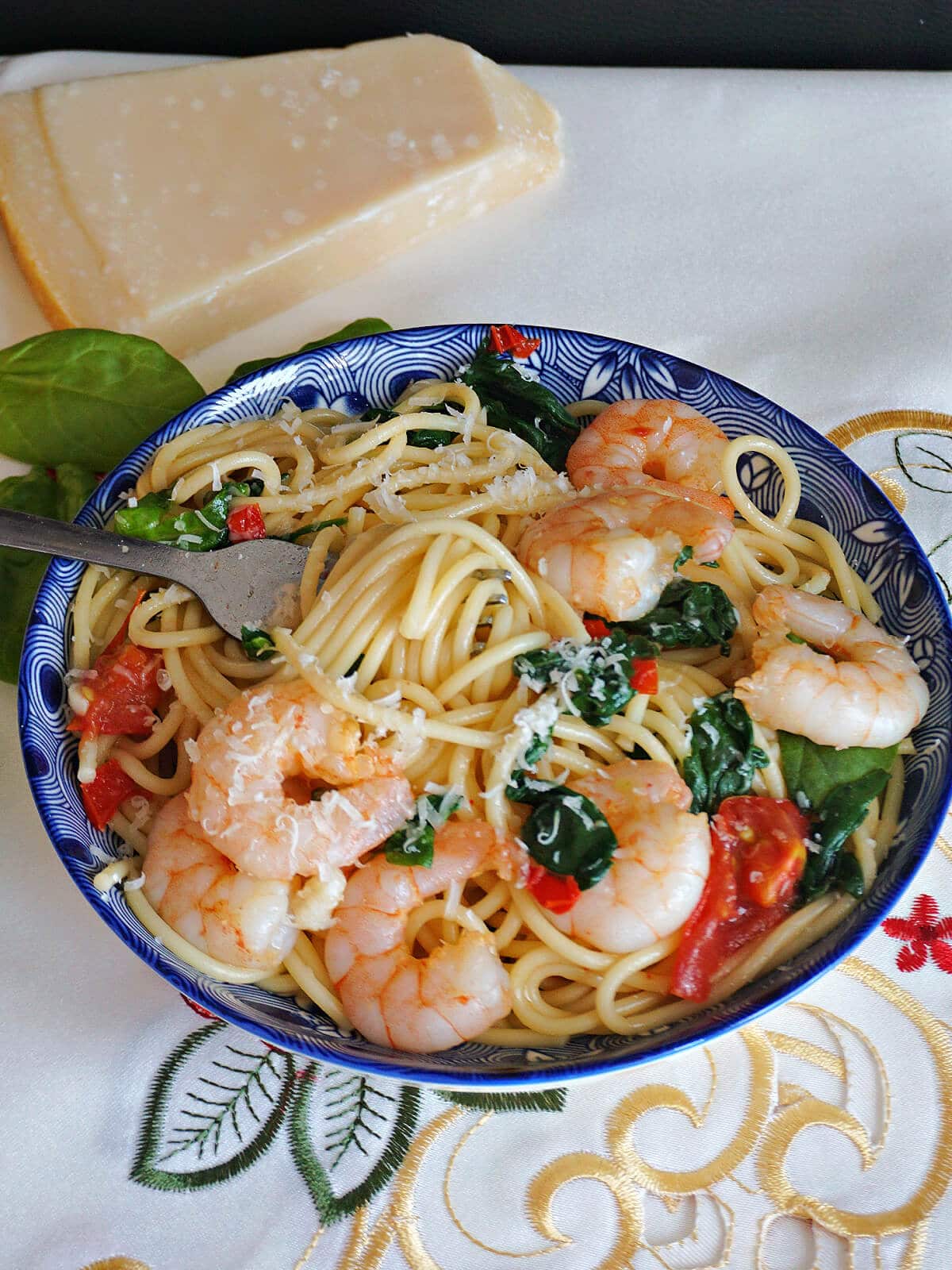 A blue bowl with spaghetti with prawns, spinach and tomatoes.