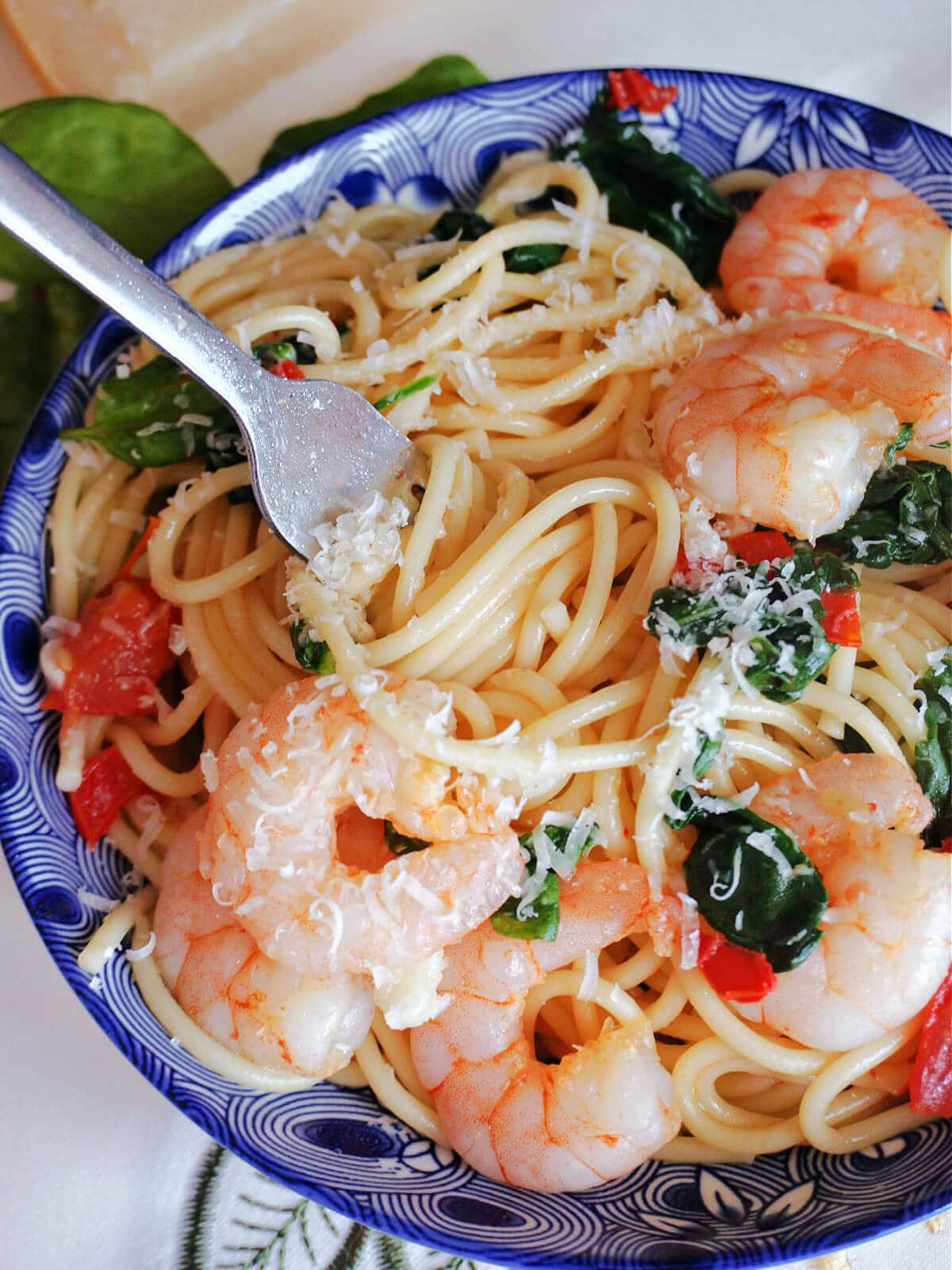 A blue bowl of pasta with prawns and spinach.