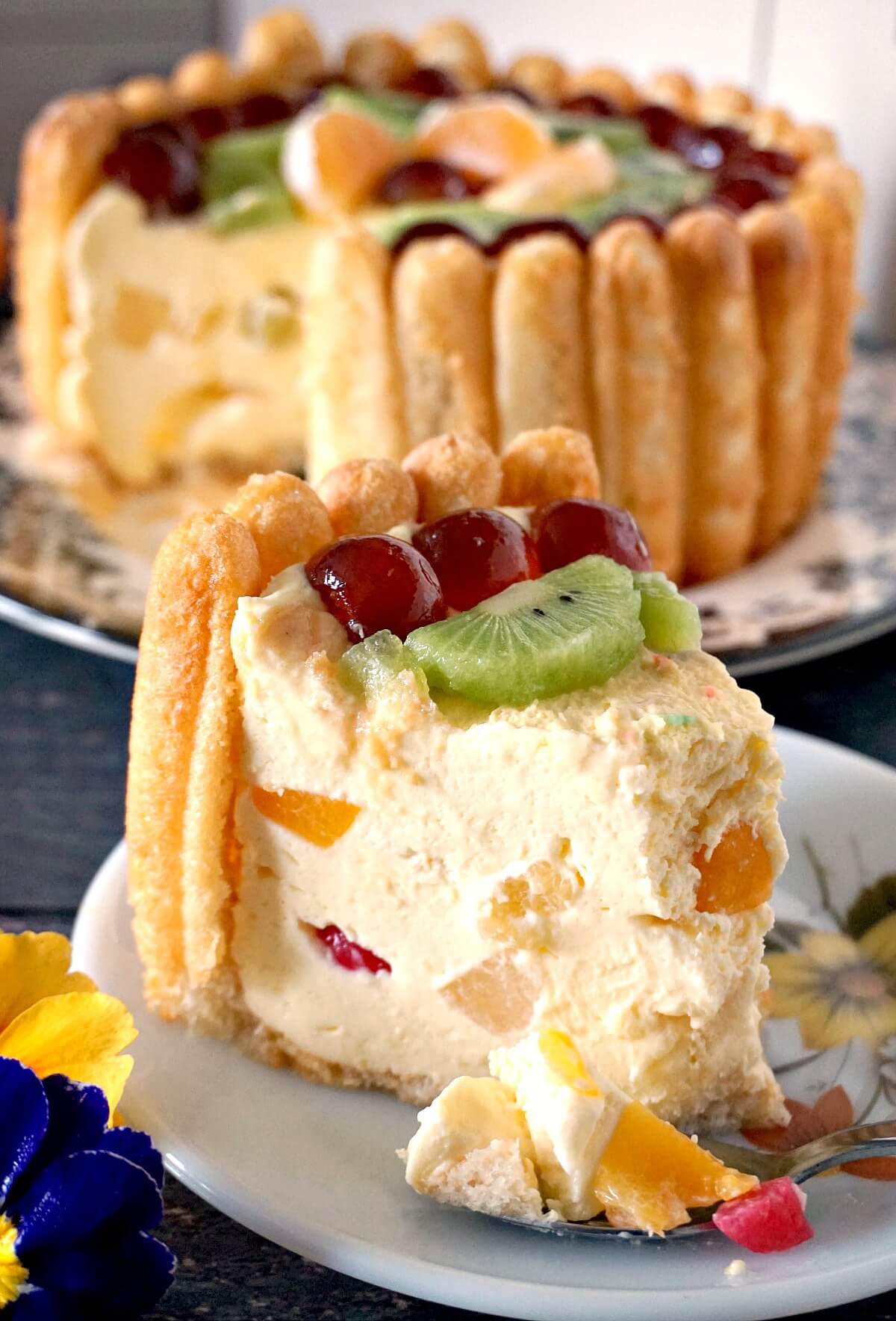 A slice of Charlotte Cake on a white plate with more cake in the background.