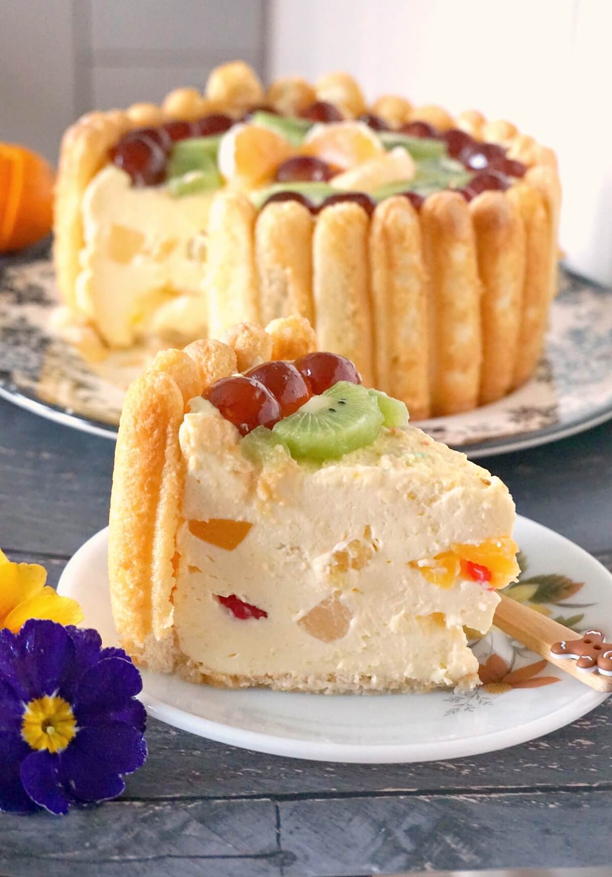 A slice of Charlotte Cake on a white plate with more cake in the background.