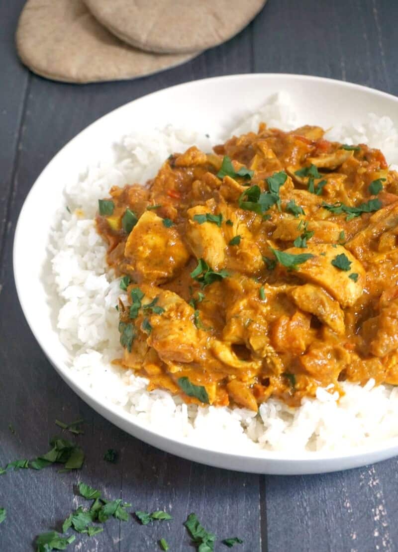 A white plate with basmati rice topped with chicken tikka masala