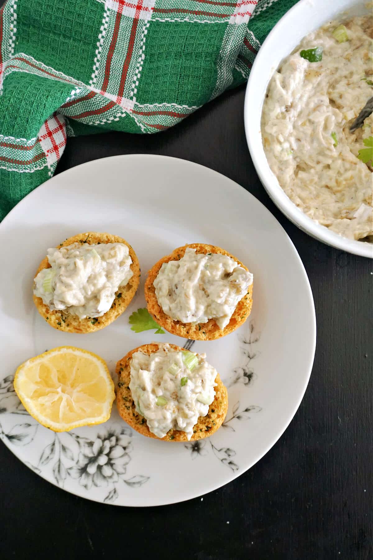 Overhead shoot of a white plate with 3 round toast bites with aubergine spread and a slice of lemon