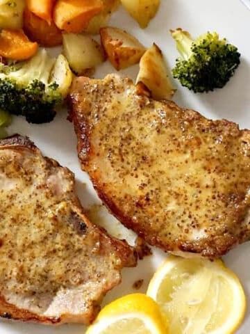 2 pork chops with veggies and 2 lemon slices on a white place