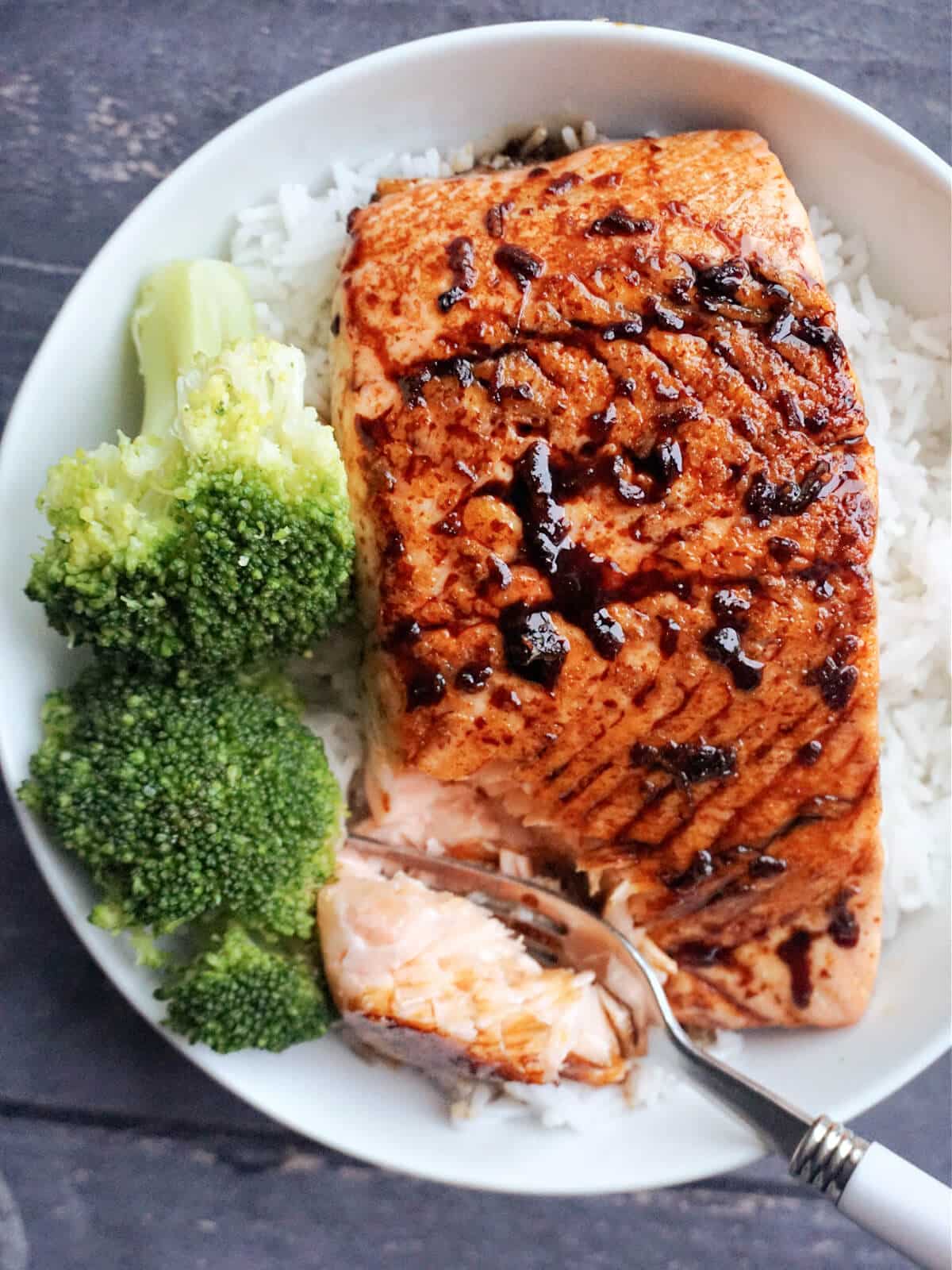 A fillet of teriyaki salmon over a bed of rice and 2 broccoli florets.