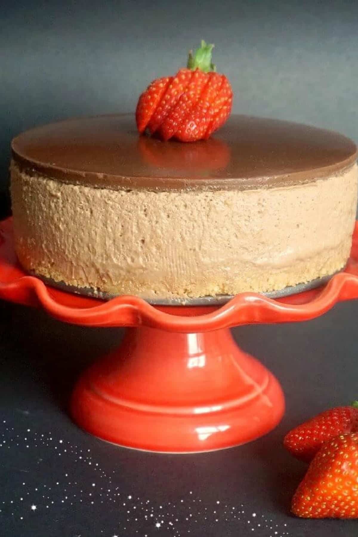 A nutella cheesecake topped with slices of strawberries on a red cake stand