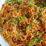 A white bowl with noodles topped with sesame seeds and parsley.