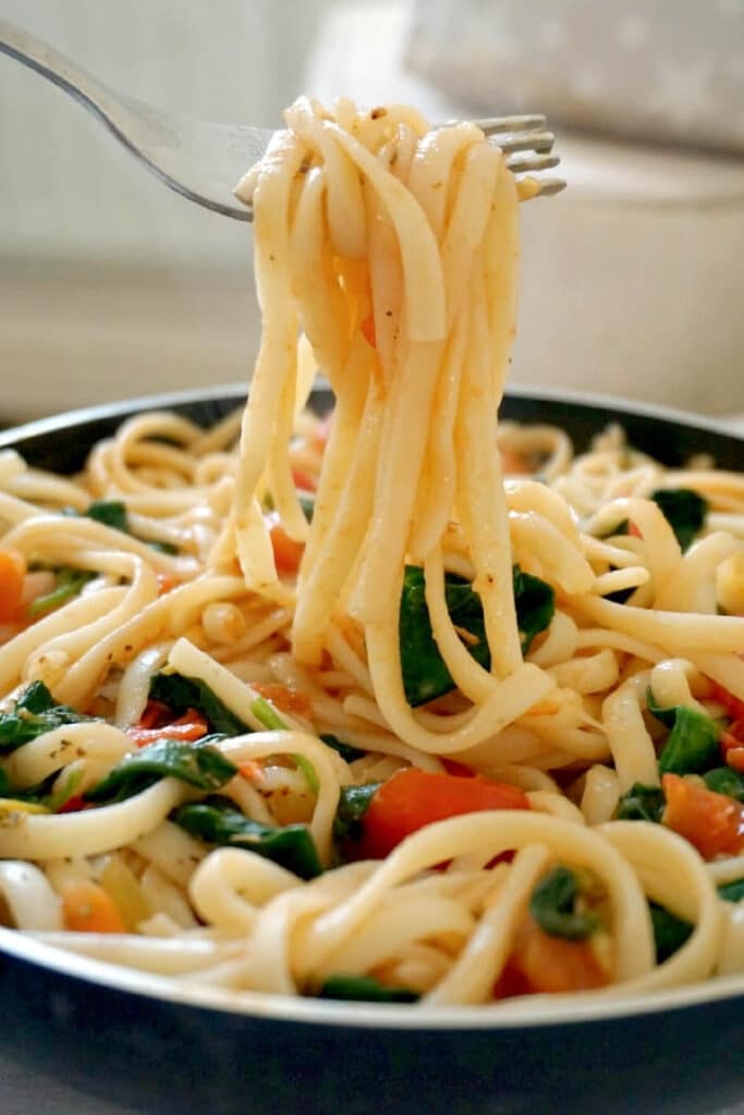 A fork full of linguini from a pan of veggie pasta