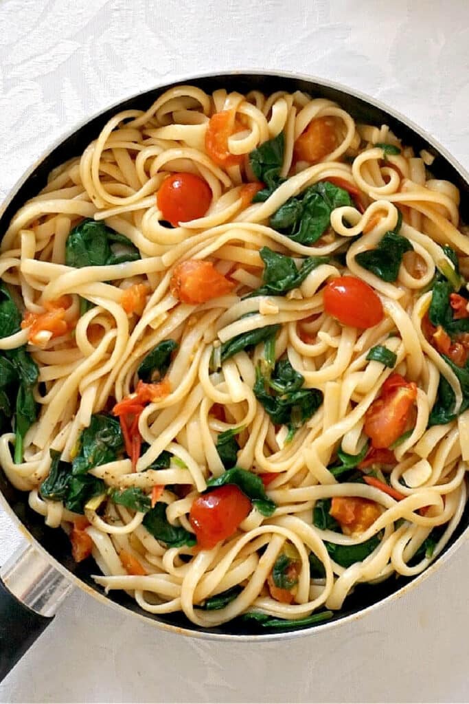 A pan with linguini, spinach and tomatoes