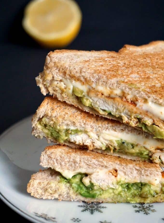 A stack of grilled chicken sandwiched with avocado and half a lemon in the background.