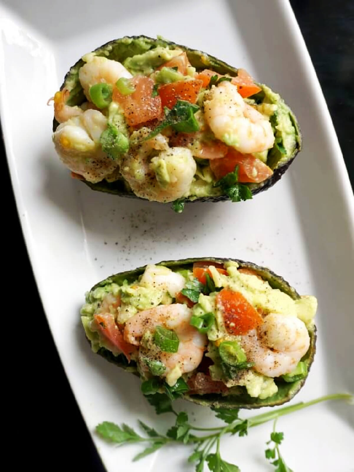 A rectangle white plate with 2 avocado skins filled with salad.