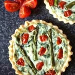 Overview shot of a Tomato, Spinach and Asparagus Tartlets with Ricotta, a tomato cut in 4 and a bit of another tartlet